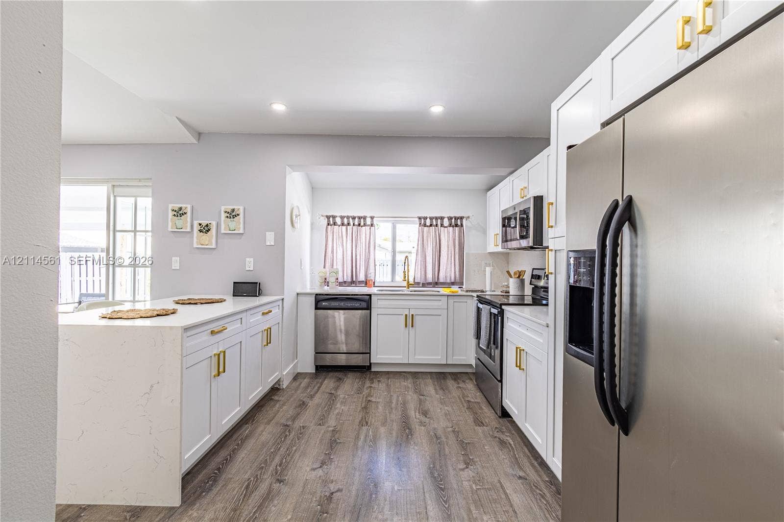 Kitchen featuring white cabinetry with gold-tone hardware, stone-finish countertops, stainless steel appliances, and wood-finish flooring