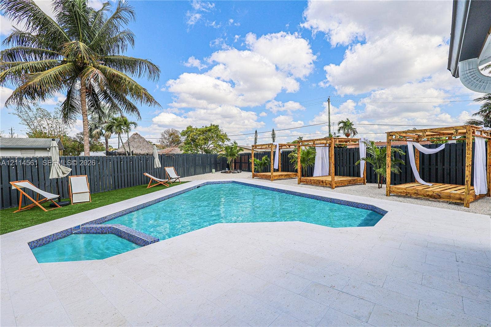 In-ground pool featuring a tile-accented spa, light-toned stone pool deck, artificial turf, and a full-perimeter privacy fence
