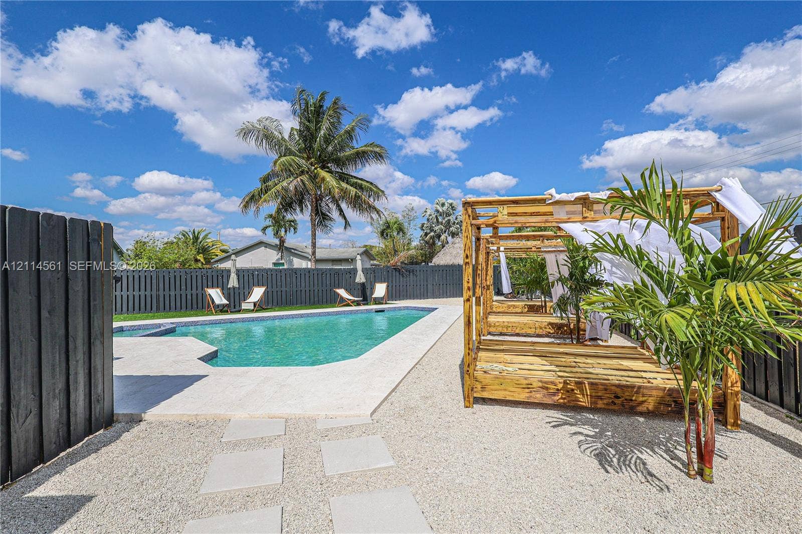 In-ground swimming pool featuring tile coping and a surrounding paver patio, complemented by a stone-covered yard and dark wood privacy fencing