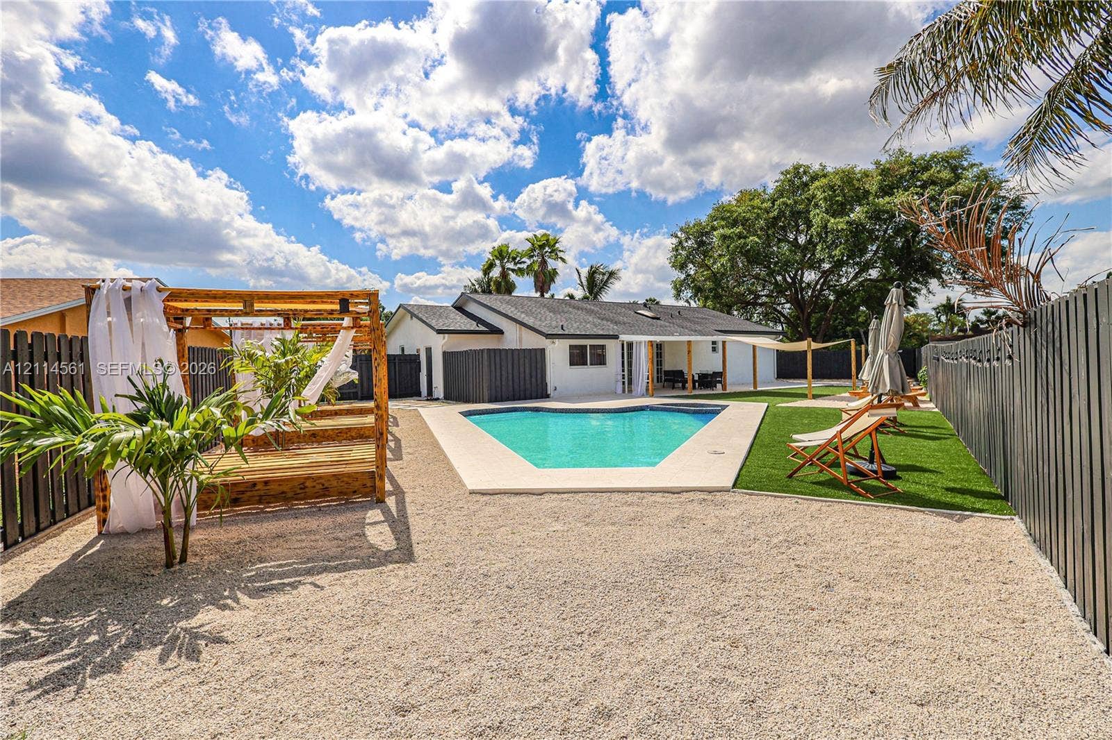 Private backyard featuring an in-ground swimming pool, custom wood pergola, gravel ground cover, artificial turf lawn, and perimeter privacy fencing