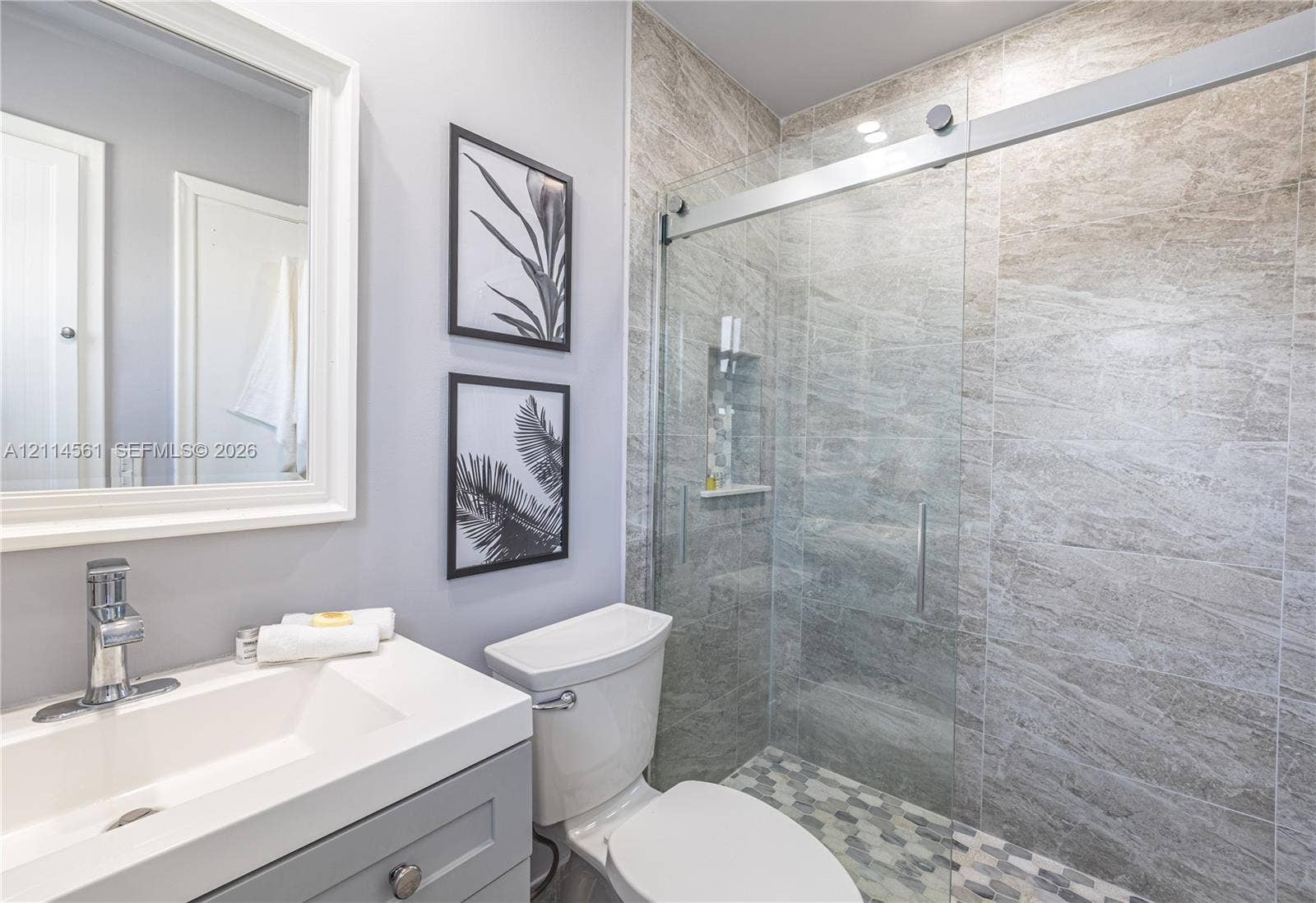 Bathroom featuring a vanity with a white countertop and chrome faucet, a walk-in shower with stone-tile surround, glass sliding door, and hexagonal floor tiling