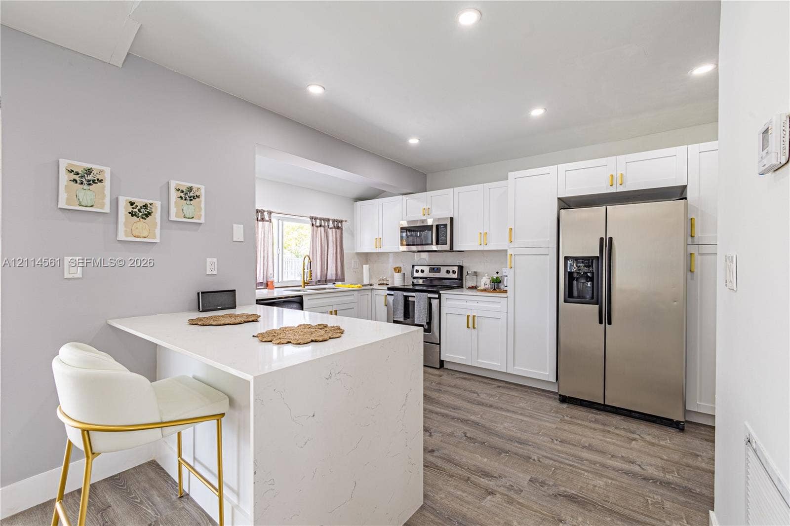 Kitchen featuring white shaker-style cabinetry, quartz countertops with waterfall edge, stainless steel appliances, recessed lighting, and wood-finish flooring