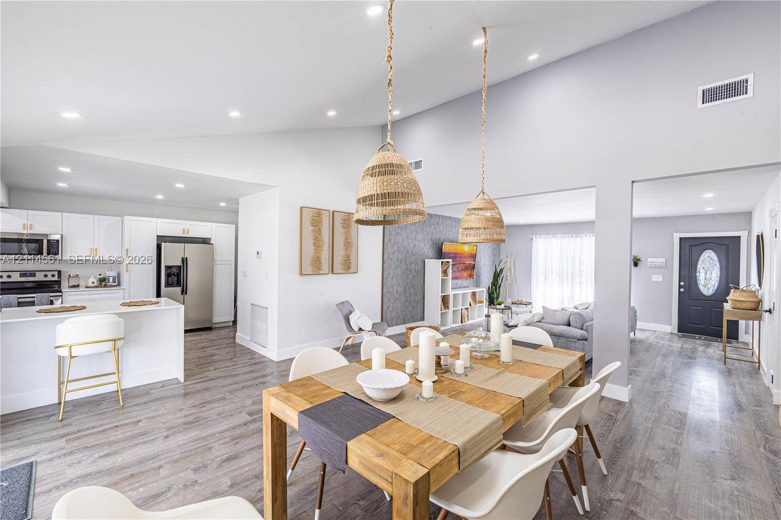 Vaulted ceilings, open-concept kitchen with white cabinetry and stainless steel appliances, wood-finish flooring, and natural-textured pendant lighting