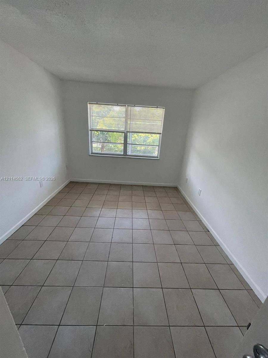 Neutral-toned square ceramic floor tiling, smooth white walls, and a large single-hung window