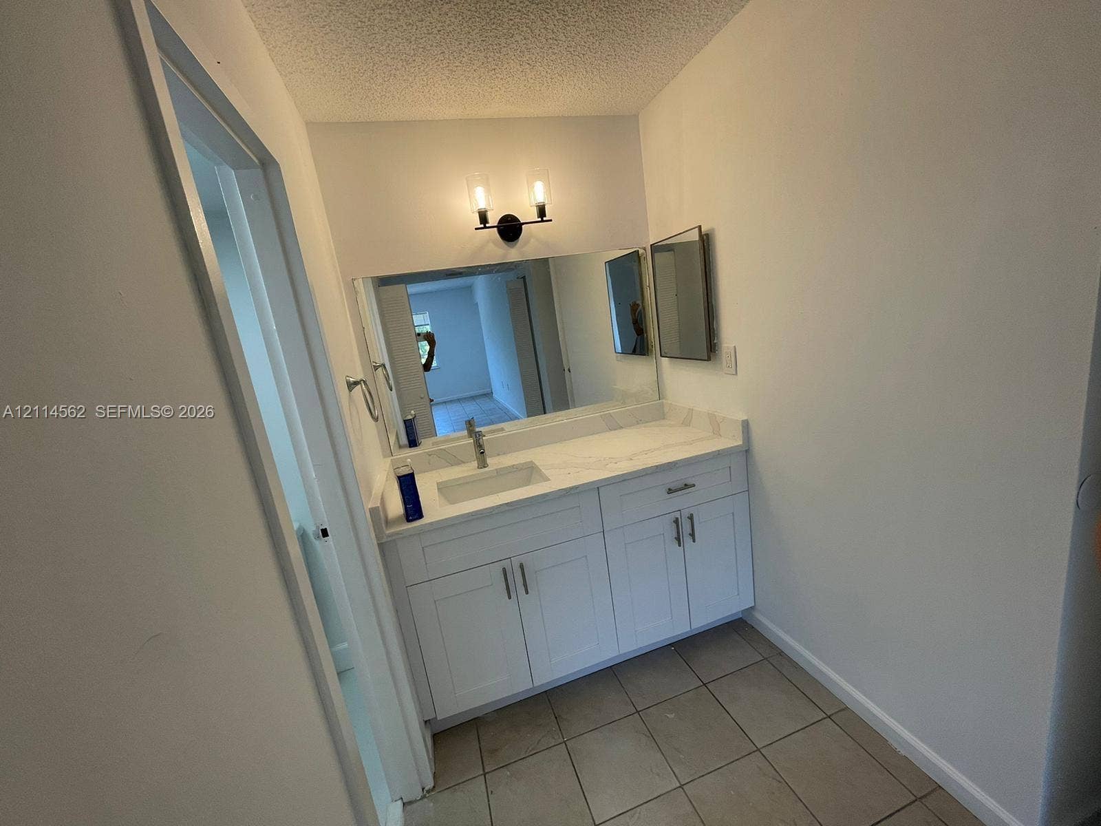 White vanity featuring shaker-style cabinetry, a stone-finish countertop with an integrated rectangular basin, a wall-to-wall mirror, and a dual-light fixture