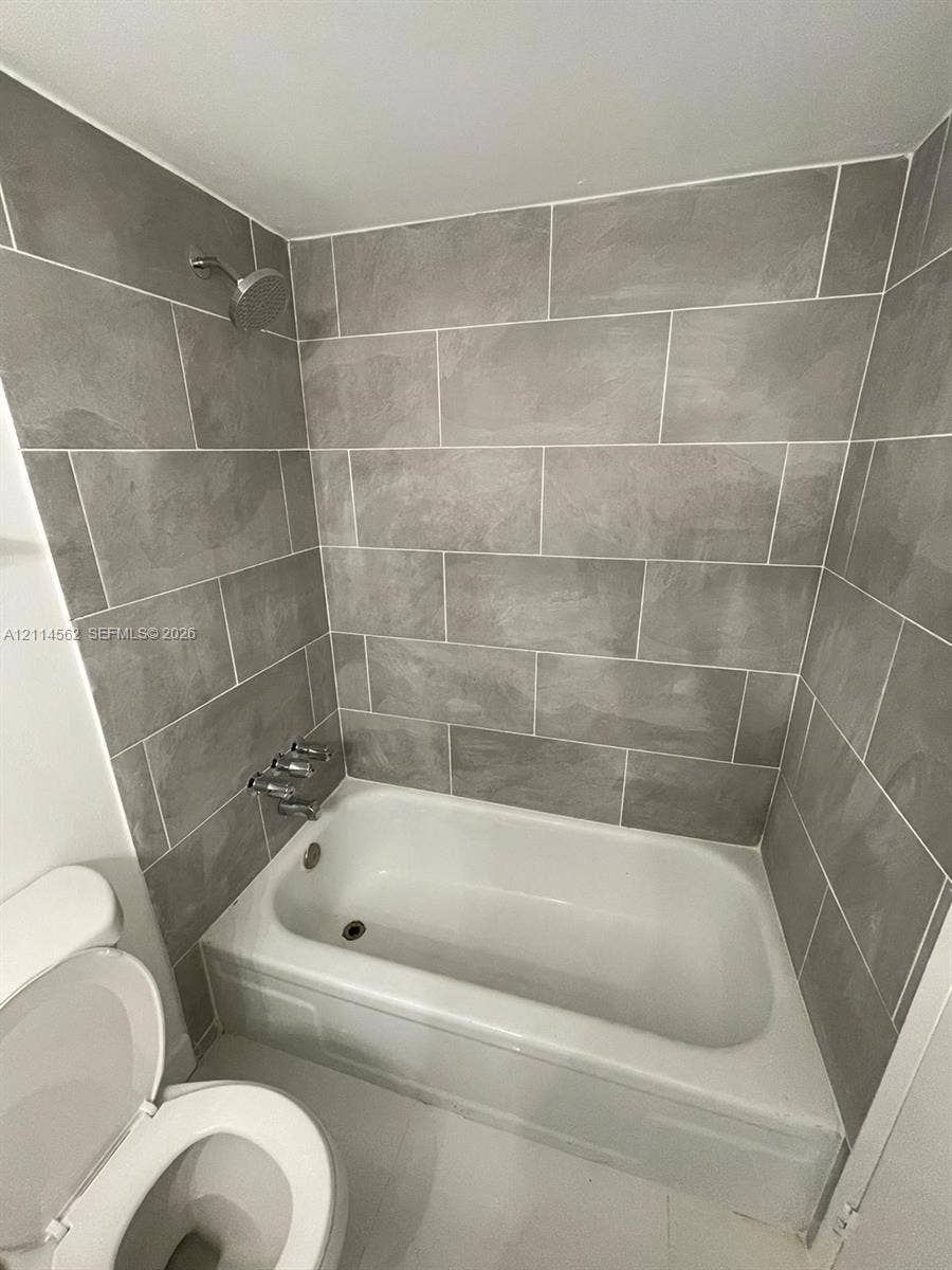 Full-height grey tile tub surround, white porcelain bathtub, chrome wall-mounted shower head, and chrome faucet hardware