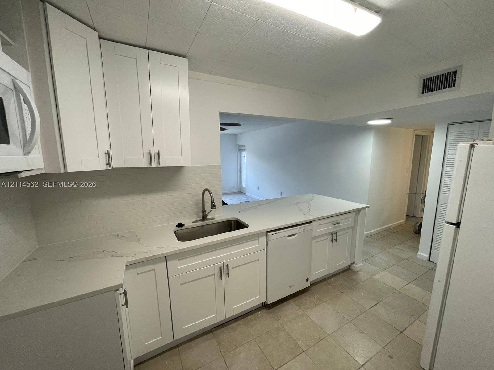 Kitchen featuring white cabinetry, quartz countertops with veining, an undermount stainless steel sink with a high-arch faucet, and a dishwasher