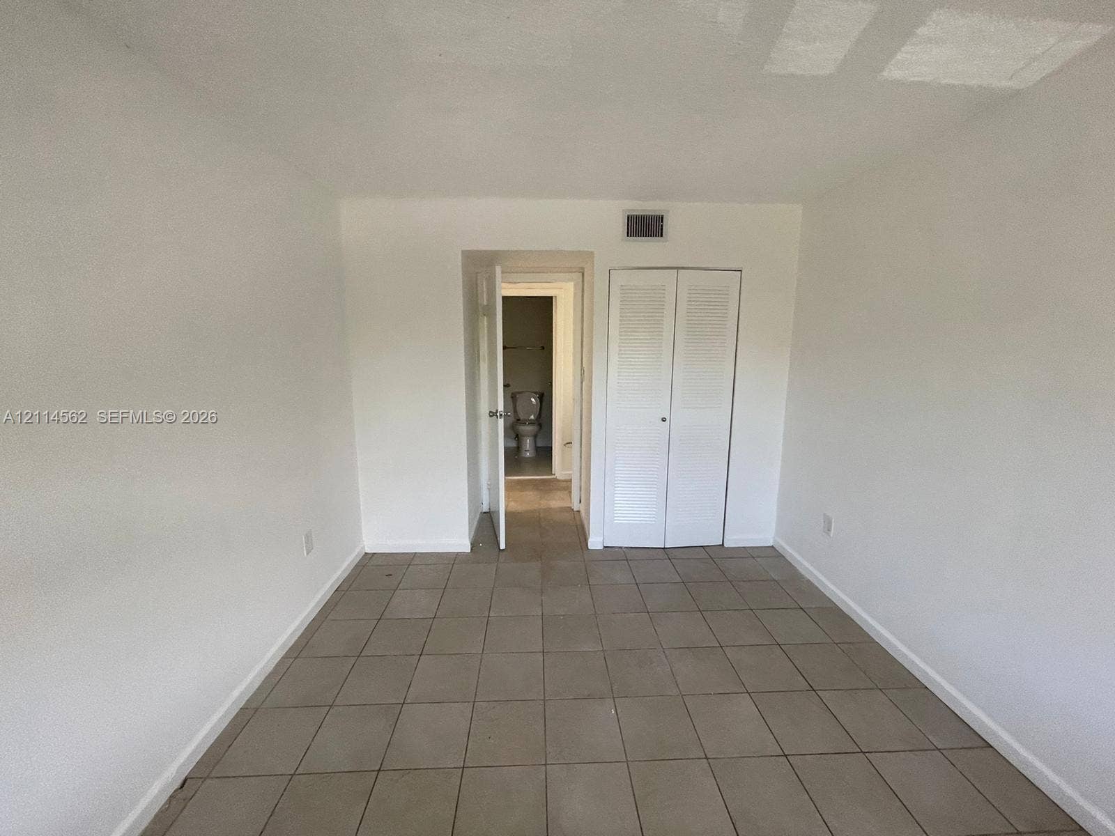 Neutral-toned tile flooring, white interior walls, and built-in closet with double louvered doors