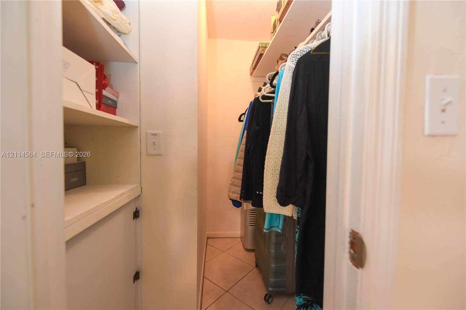 Storage closet featuring built-in shelving, overhead racks, and tile flooring