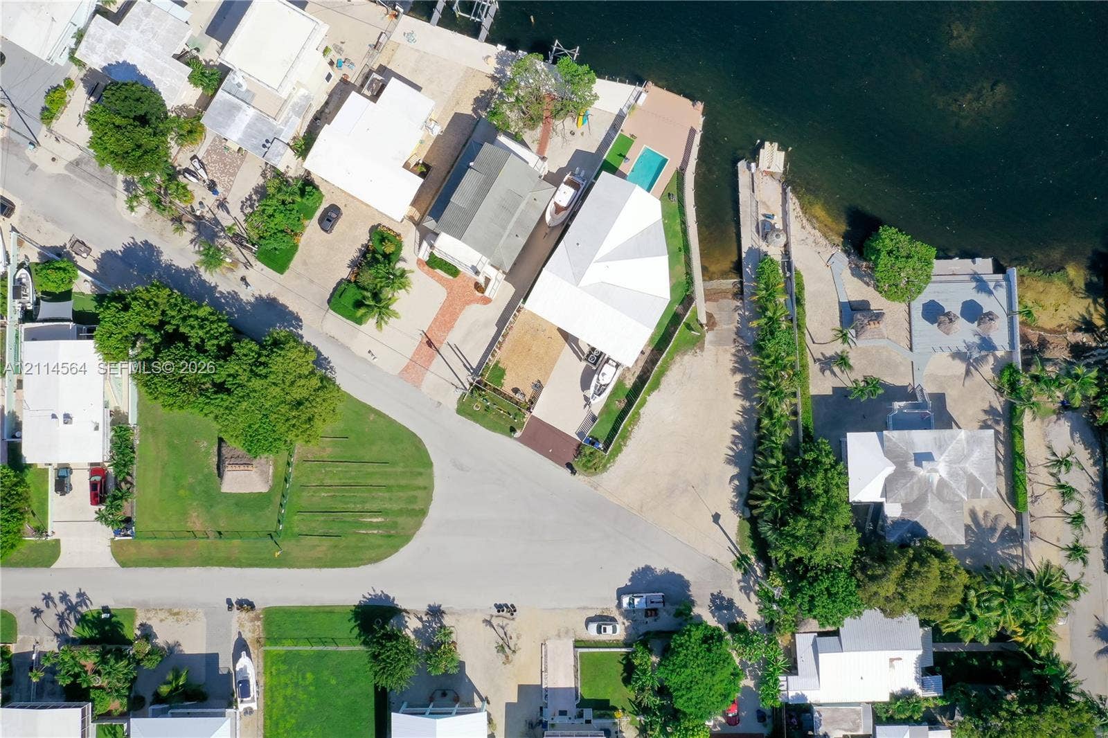 Aerial perspective of waterfront property featuring a private boat slip, concrete seawall, in-ground swimming pool, and paved driveway