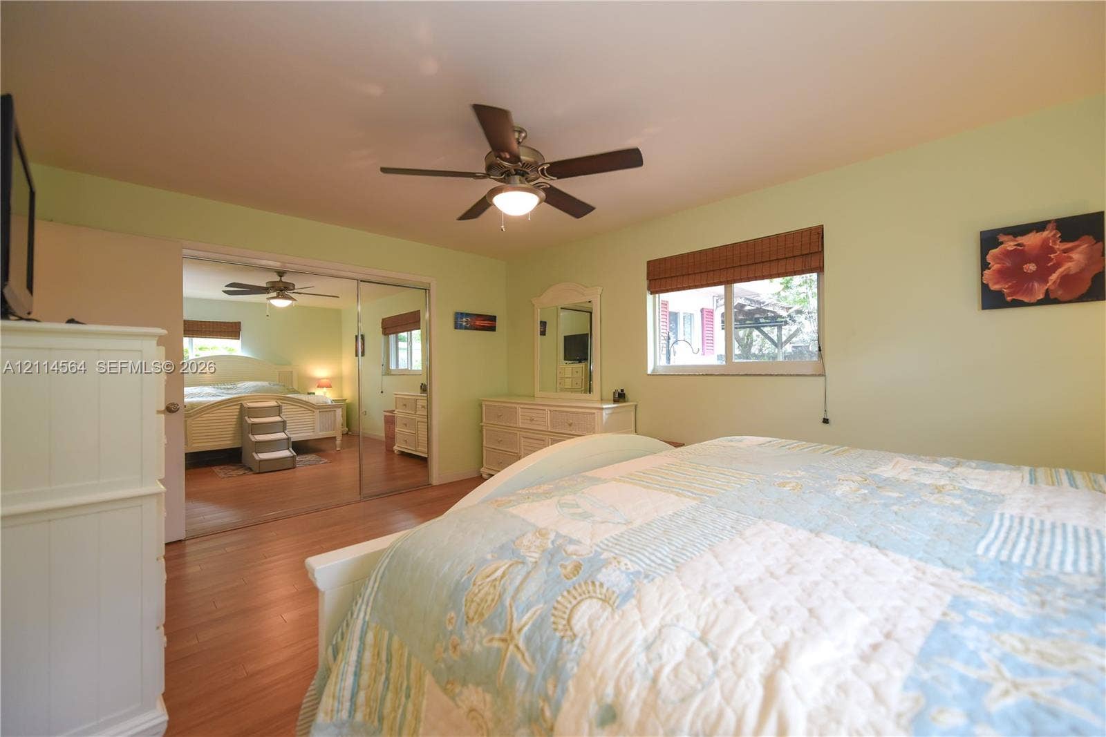 Wood-finish flooring, ceiling fan with integrated lighting, mirrored sliding closet doors, and woven wood window treatments
