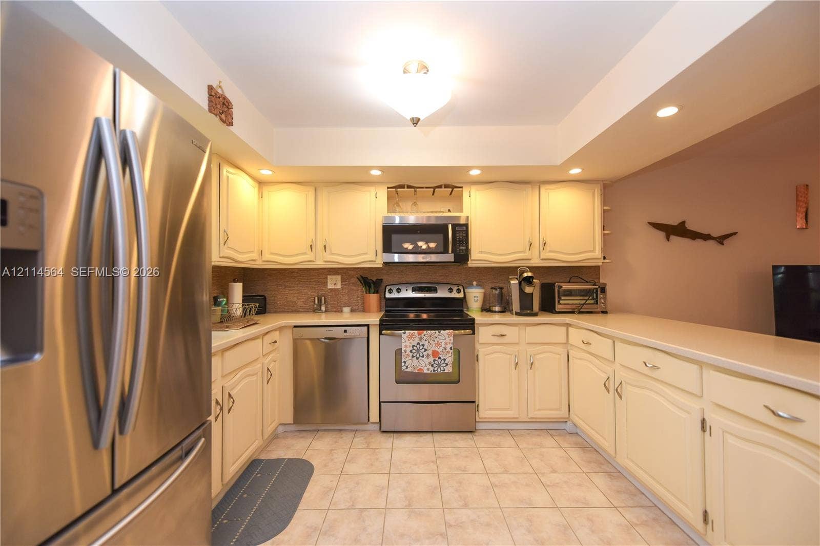 Kitchen featuring stainless steel appliances, raised-panel cabinetry, solid-surface countertops, recessed lighting, and tile flooring