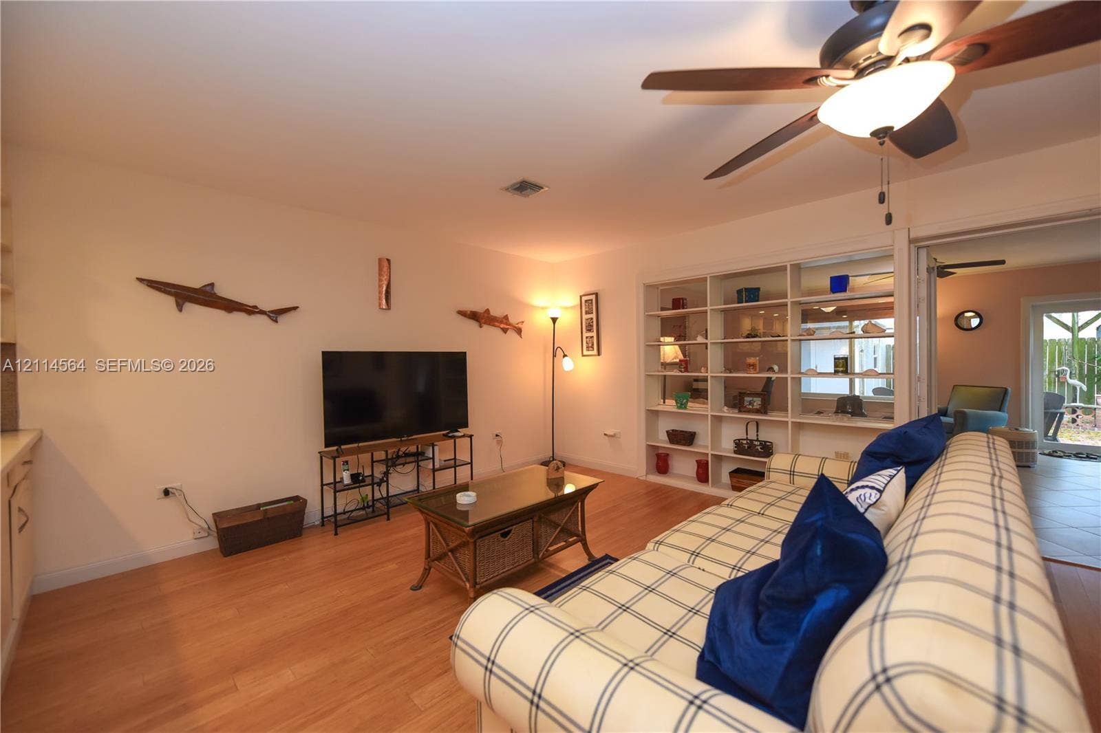 Living area featuring wood-finish flooring, a ceiling fan with integrated lighting, and built-in floor-to-ceiling shelving