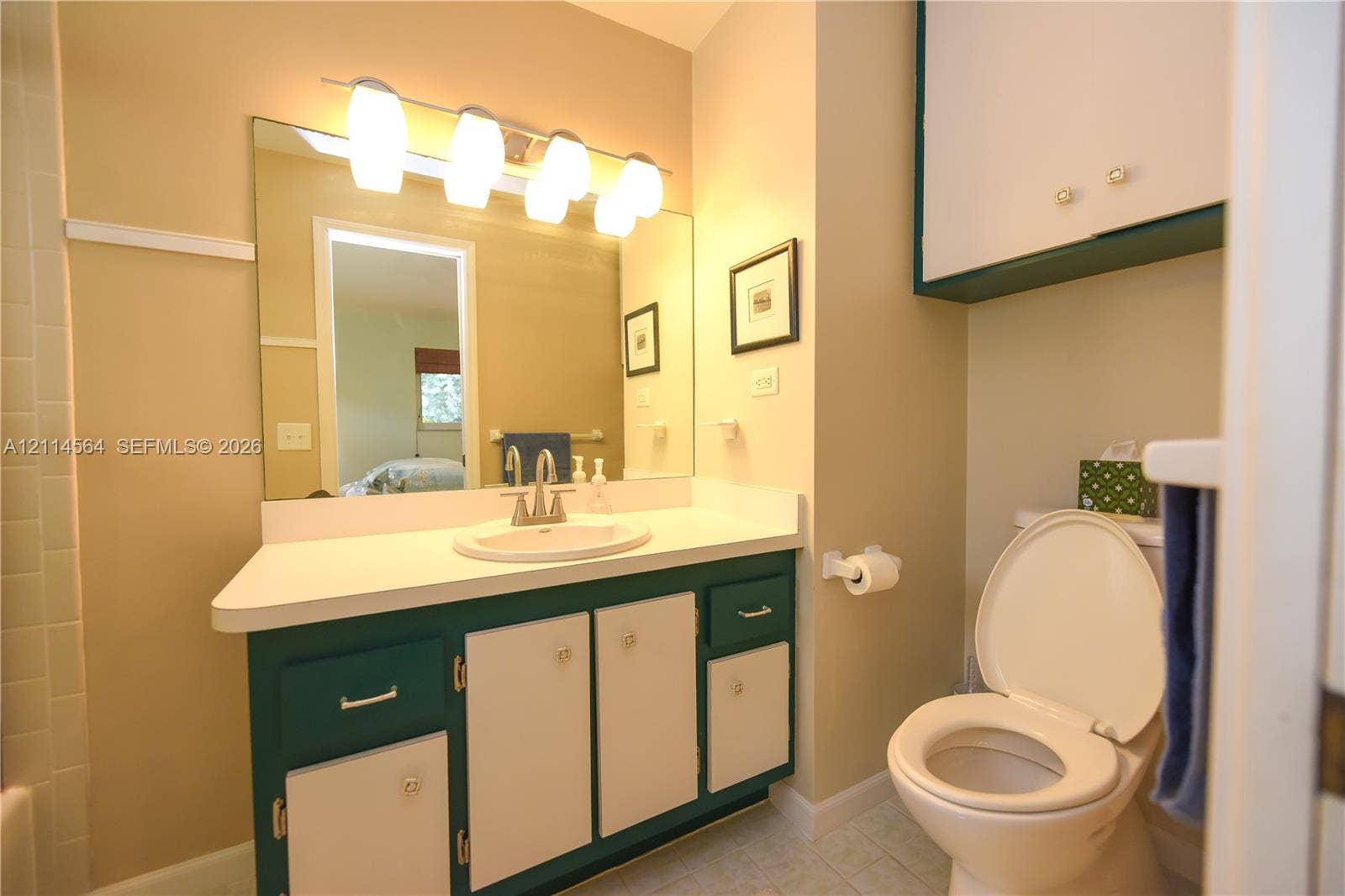 Bathroom featuring a vanity with dual-tone cabinetry, solid surface countertop with integrated basin, four-light vanity fixture, and large wall-mounted mirror