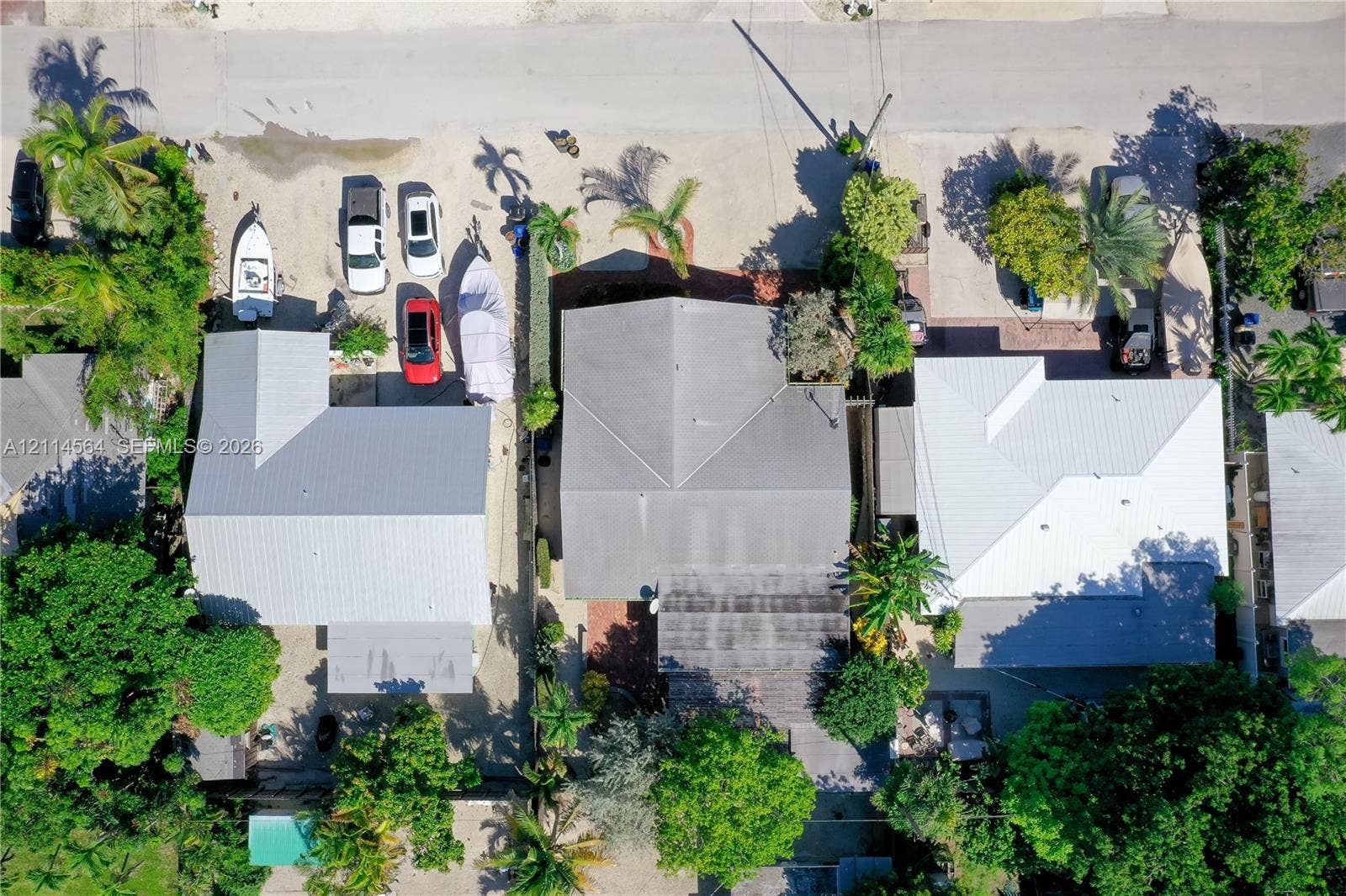 Aerial view featuring a metal roof system, paved driveway, mature trees, and established landscaping