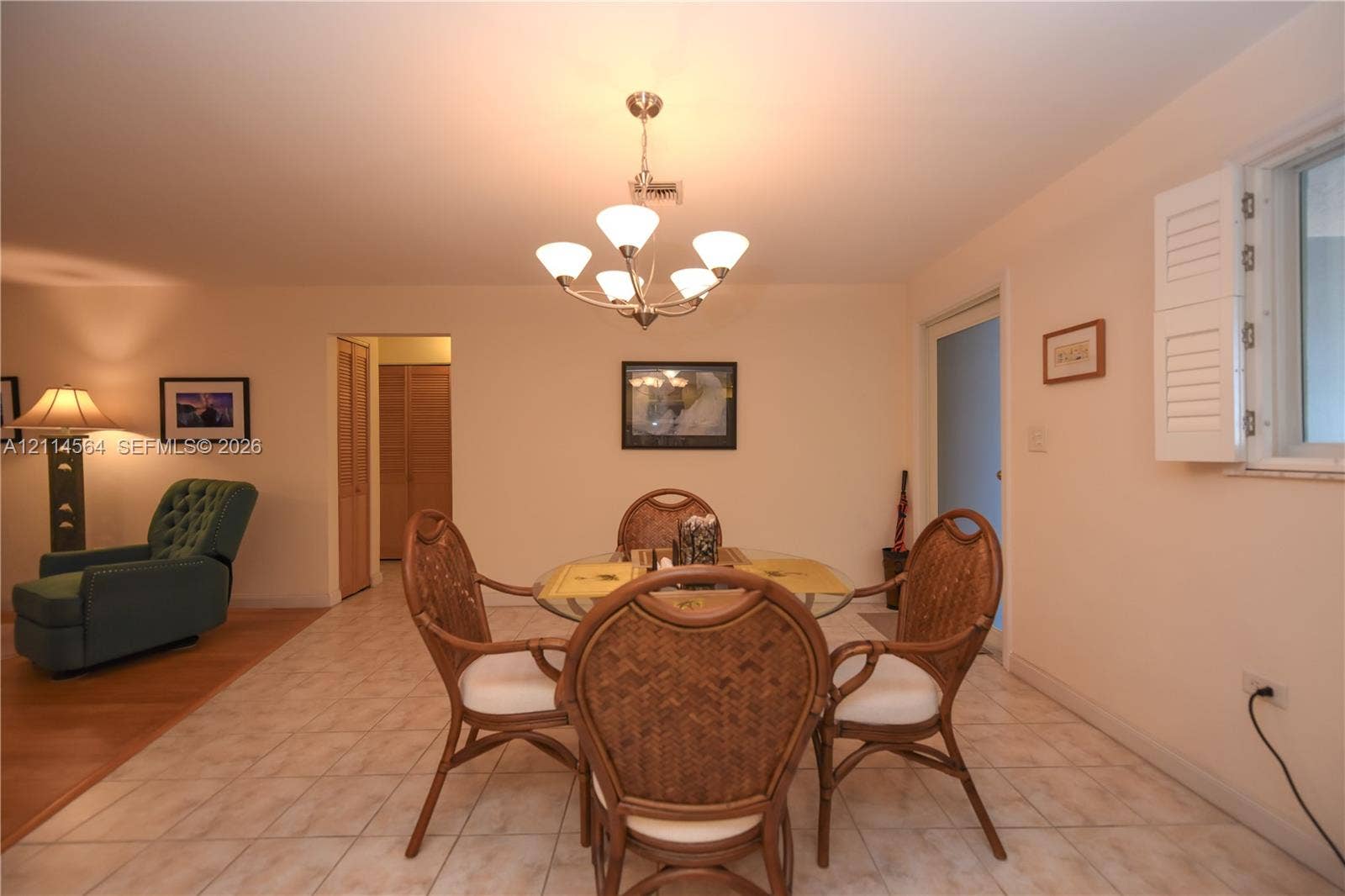 Open-concept area featuring neutral wall tones, large-format tile flooring, a multi-arm metallic chandelier, and plantation shutters