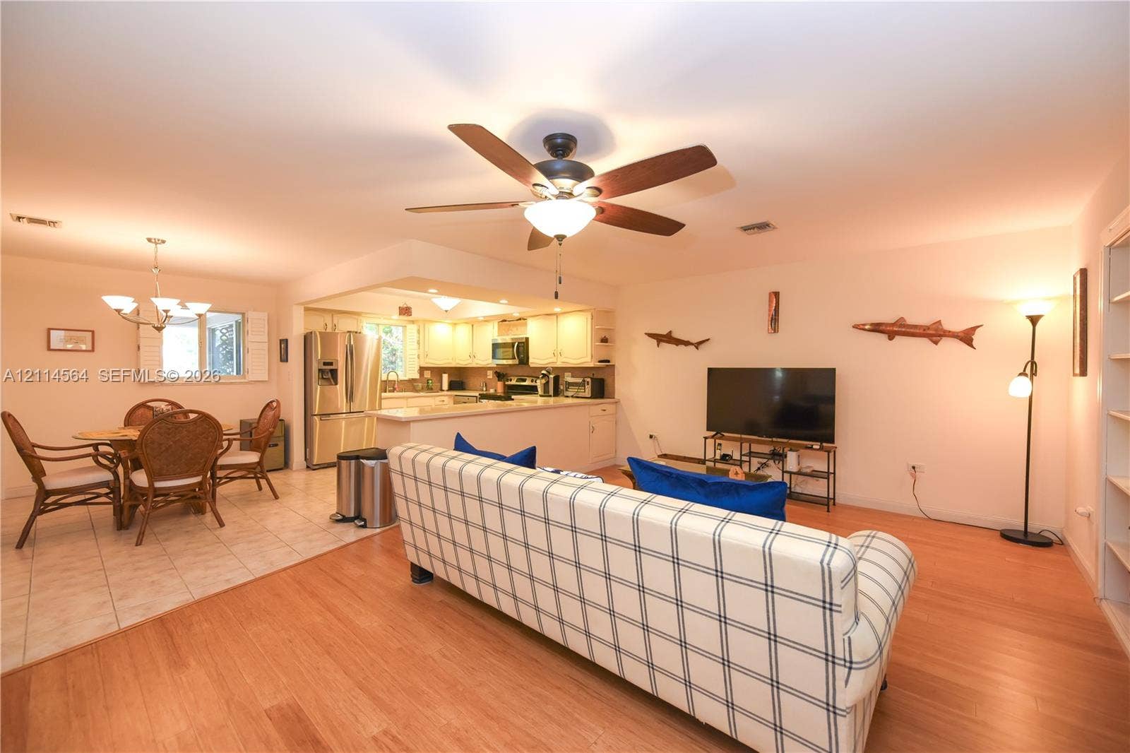 Open-concept area featuring wood-finish flooring, tile flooring, kitchen cabinetry, and a ceiling-mounted fan with integrated lighting
