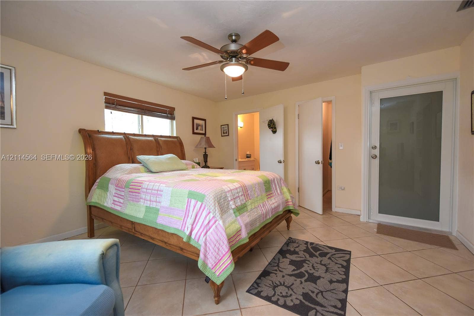 Room featuring neutral-toned ceramic tile flooring, a central ceiling fan with integrated lighting, and a doorway with a frosted glass panel insert