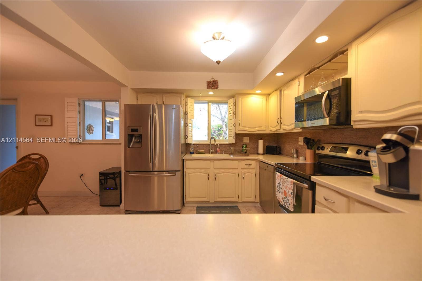 Kitchen featuring stainless steel appliances, off-white cabinetry, solid surface countertops, a dual-basin sink, and recessed lighting