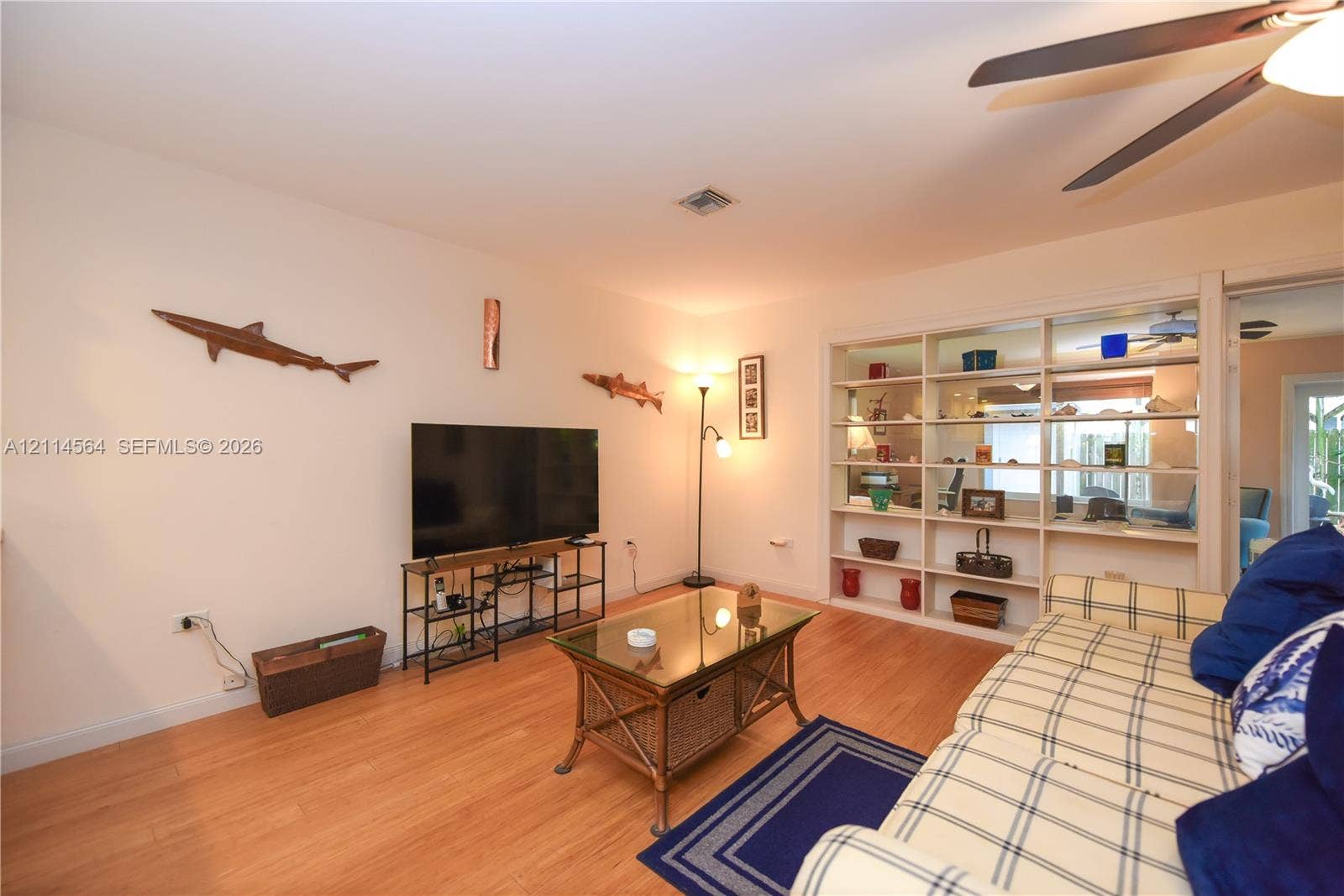 Living area featuring wood-finish flooring, recessed ceiling lighting, a dedicated ceiling fan, and built-in floor-to-ceiling shelving