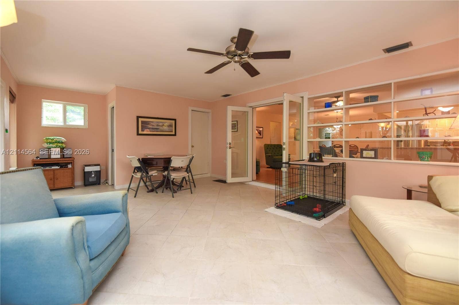 Open-concept interior featuring large-format tile flooring, a ceiling fan, double French doors, and a built-in multi-level display shelving unit