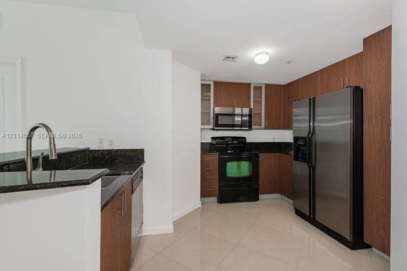 Kitchen featuring wood-finish cabinetry, stone countertops, stainless steel appliances, and tile flooring