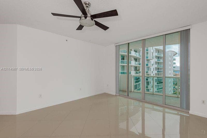 Neutral-toned tile flooring, floor-to-ceiling glass sliding doors, and a ceiling-mounted fan with integrated light fixture