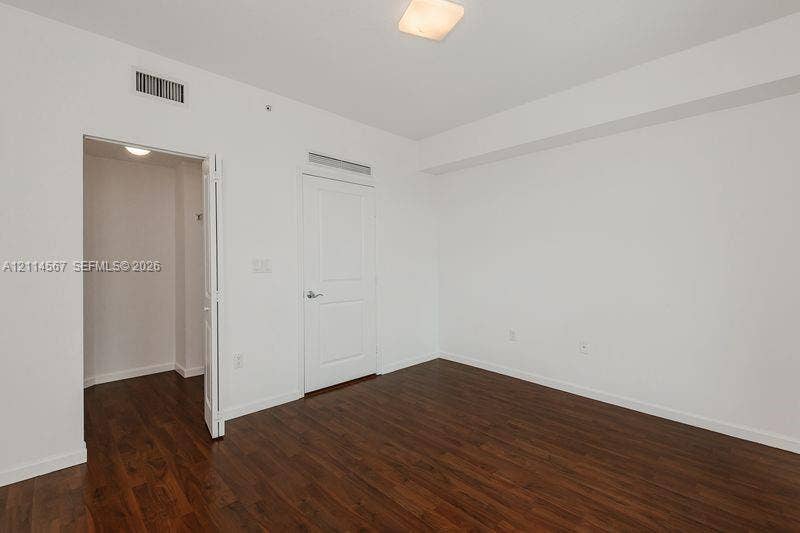 Interior room featuring wood-finish flooring, white walls, a multi-panel door, and a flush-mount light fixture