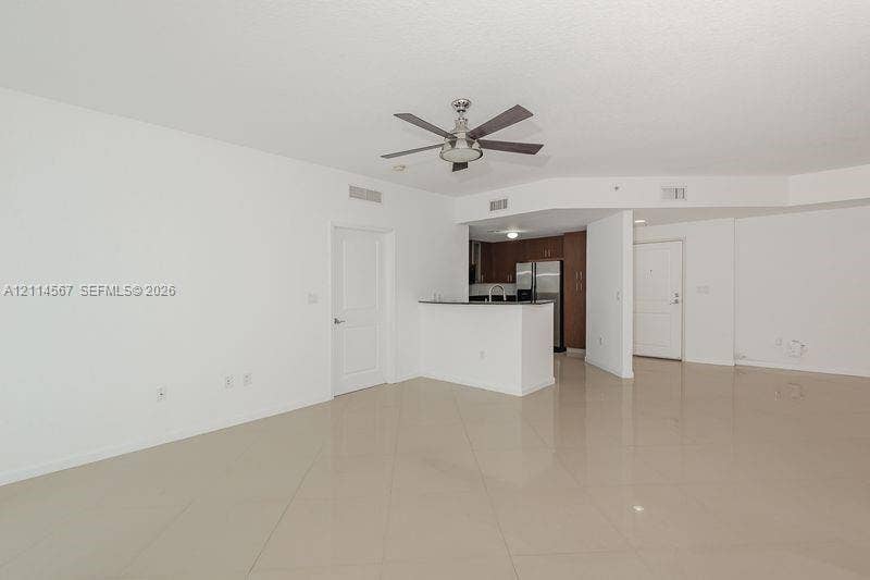 Open-concept interior featuring large-format tile flooring, a central ceiling fan, a breakfast bar with stone-surface countertop, and wood-finish cabinetry
