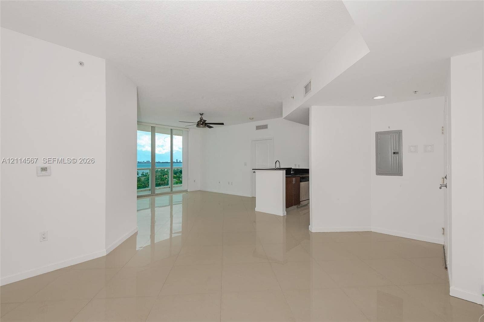 Open-concept interior featuring large-format tile flooring, floor-to-ceiling glass windows, a ceiling fan, and a kitchen peninsula with dark countertops and wood-finish cabinetry
