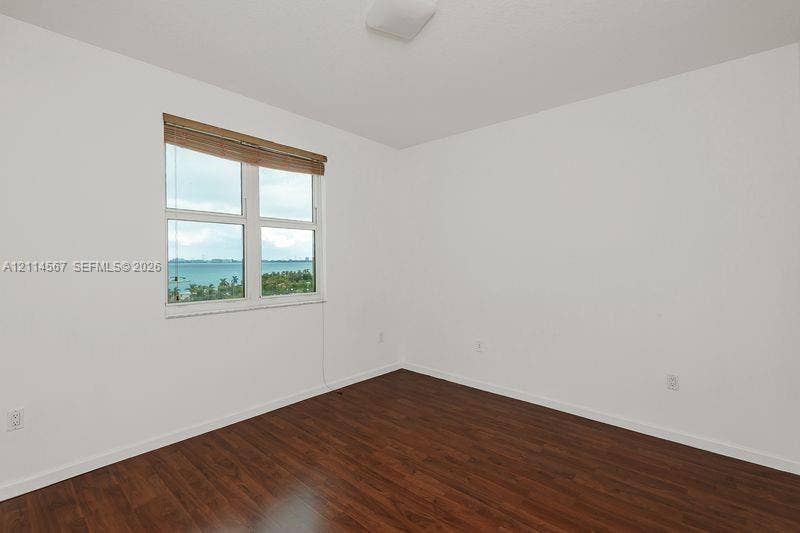 Interior space featuring wood-finish flooring, white walls, and a window with water and vegetation scenery