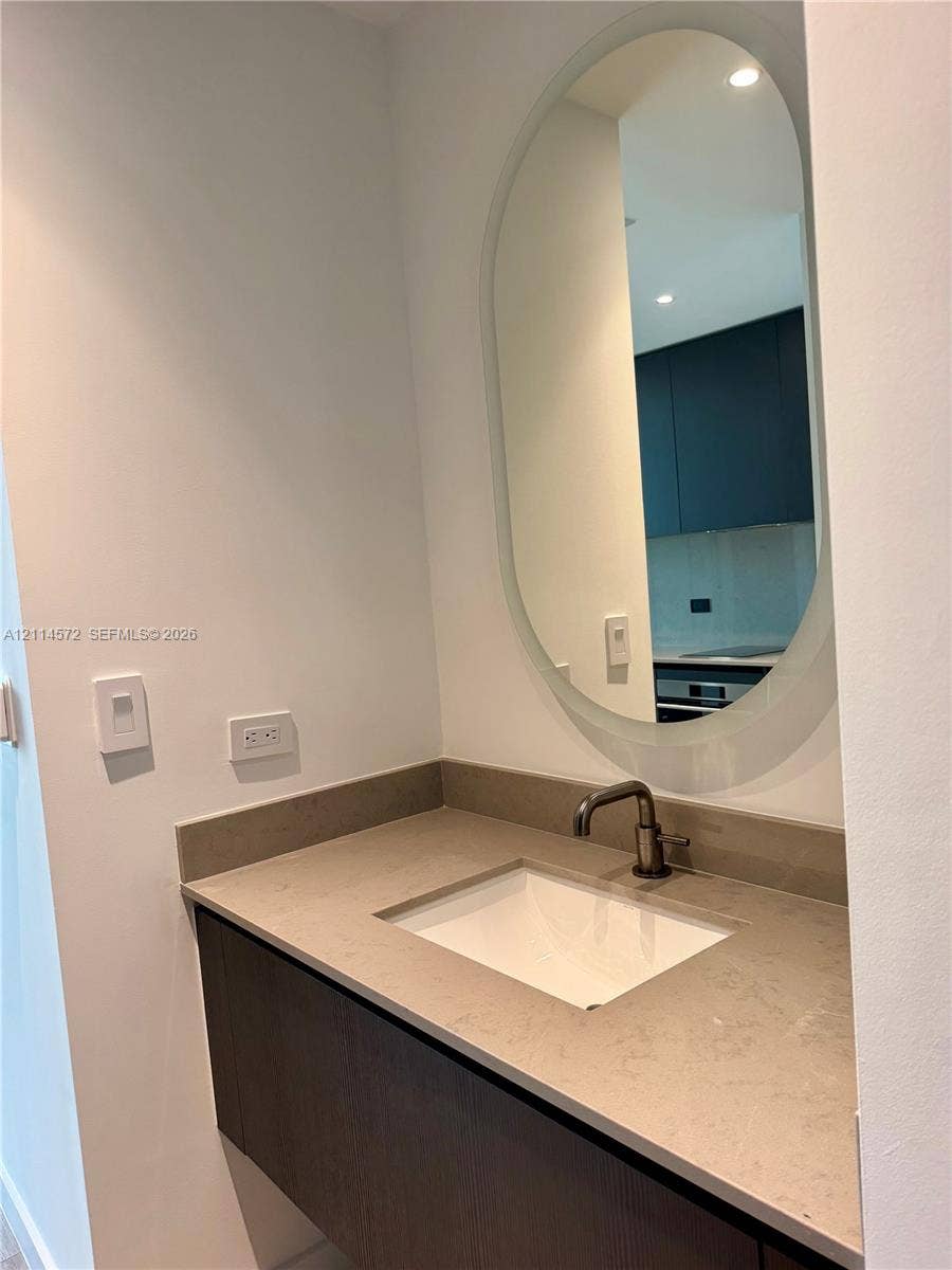 20 NE 11, #3312B, Miami, FL 33132 Floating vanity with a stone countertop, undermount sink, dark-finished faucet, and oval wall mirror