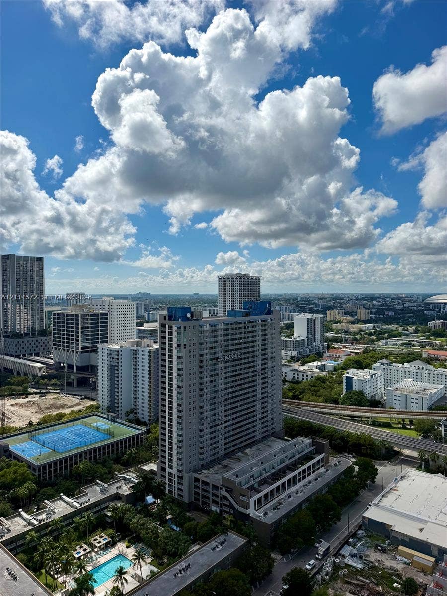 20 NE 11, #3312B, Miami, FL 33132 Aerial perspective of urban landscape featuring high-rise architecture, a multi-story parking structure, a blue-surface tennis court, and a rectangular ground-level pool