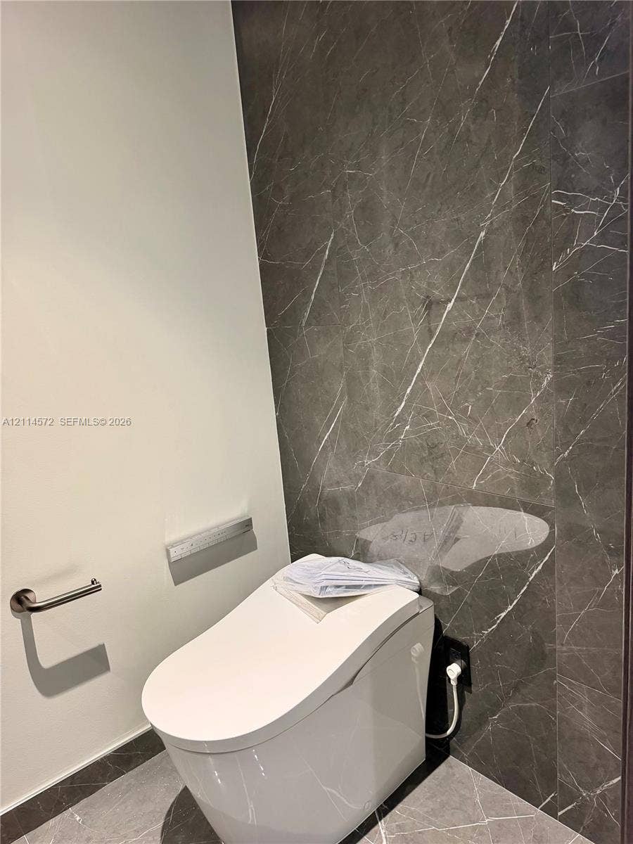 20 NE 11, #3312B, Miami, FL 33132 Modern restroom featuring full-height charcoal-toned stone wall cladding, matching stone floor tile, and a contemporary low-profile toilet with integrated flush system and brushed nickel hardware
