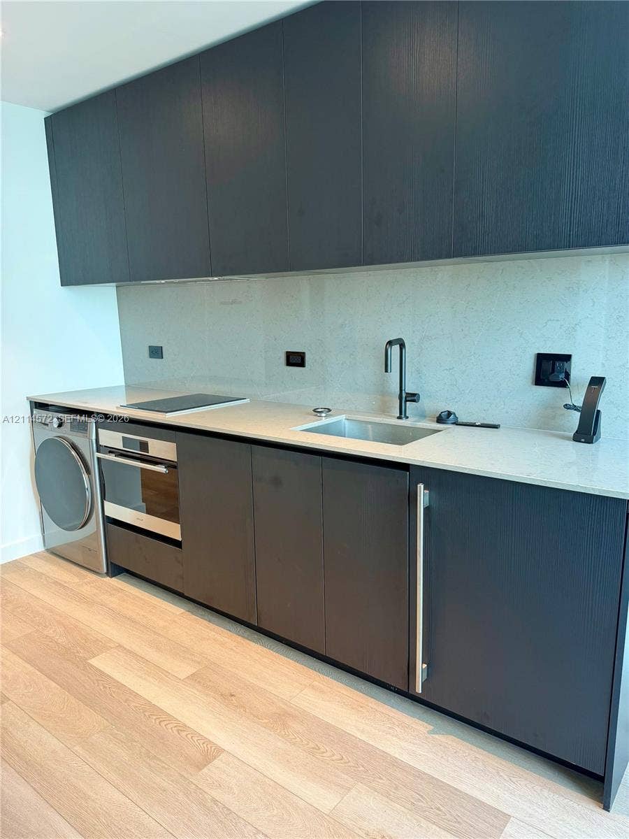 20 NE 11, #3312B, Miami, FL 33132 Modern cabinetry with flat-panel doors, light-toned stone-finish countertops, integrated stainless steel appliances, under-mount sink with matte black faucet, and wide-plank wood-finish flooring