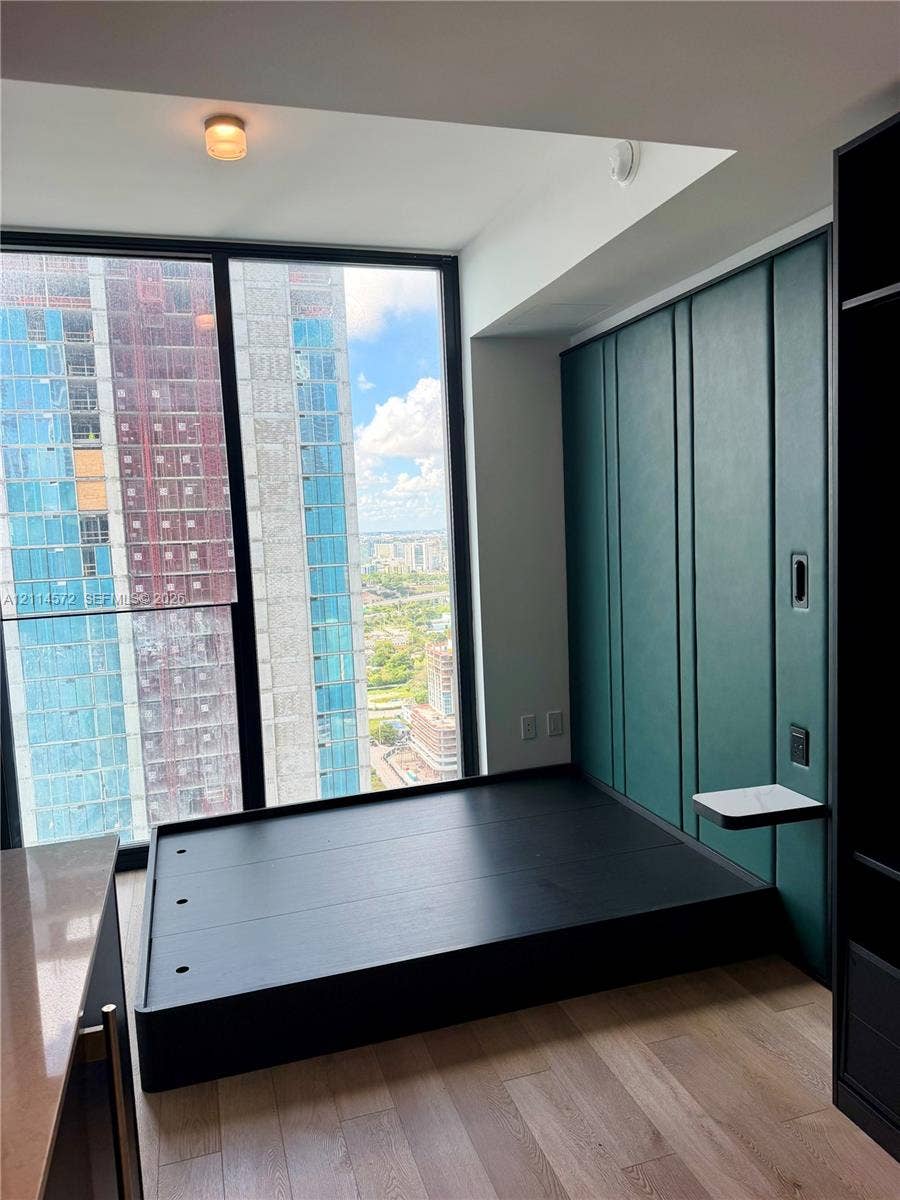 20 NE 11, #3312B, Miami, FL 33132 Floor-to-ceiling windows, custom green paneled wall with integrated shelving, built-in elevated platform, and wood-finish flooring