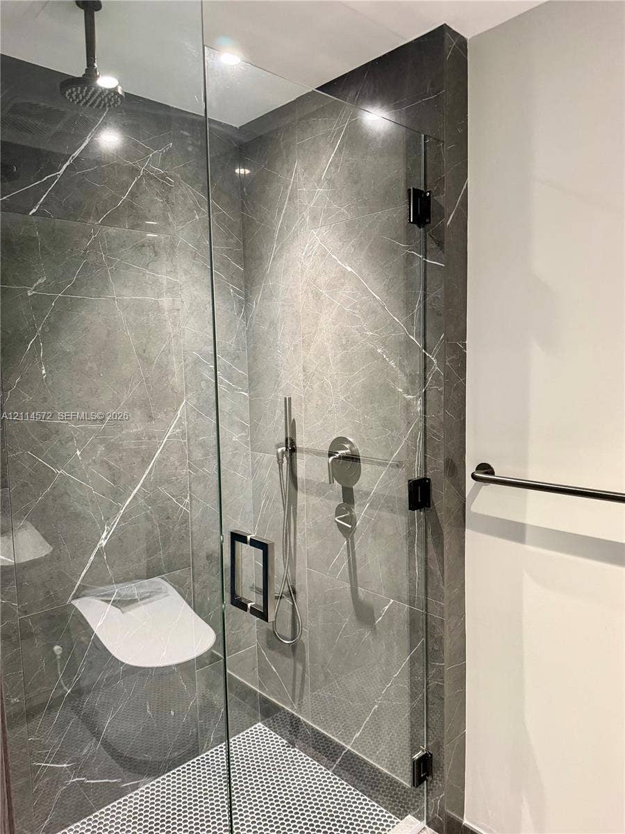 20 NE 11, #3312B, Miami, FL 33132 Walk-in shower featuring large-format stone-look wall tiles, mosaic floor tiling, frameless glass enclosure, ceiling-mounted rainfall showerhead, and adjustable hand-held sprayer