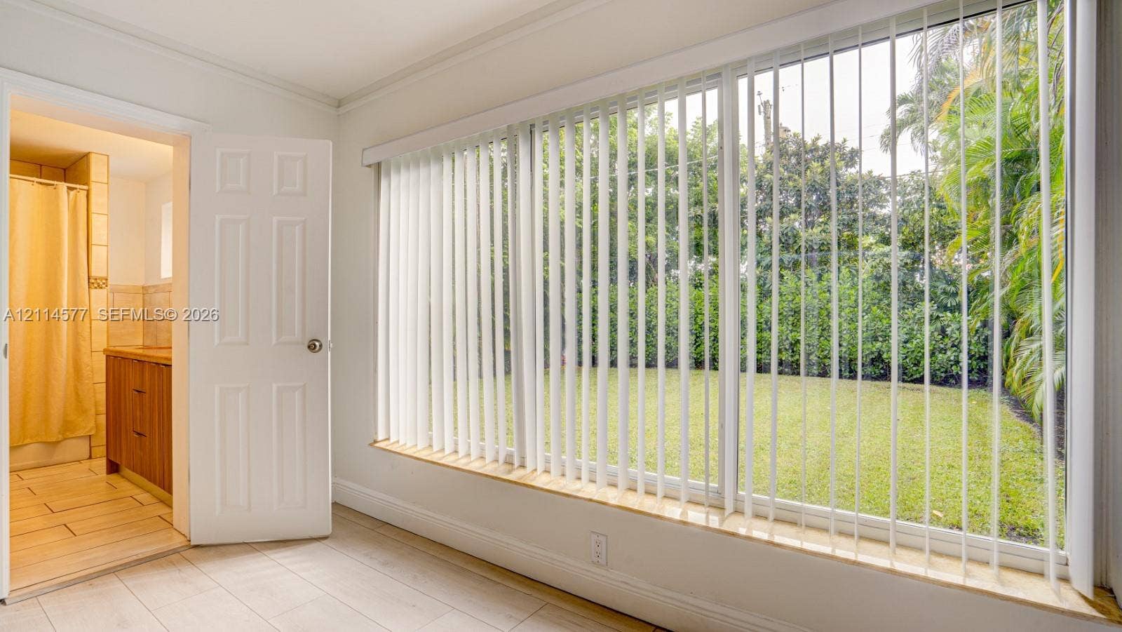 311 SW 38th Court, #0, Miami, Miami, FL 33134 Expansive multi-pane window with vertical blinds, light-toned tile flooring, and a solid-core interior door leading to a bathroom featuring a wooden vanity and ceramic wall tiling