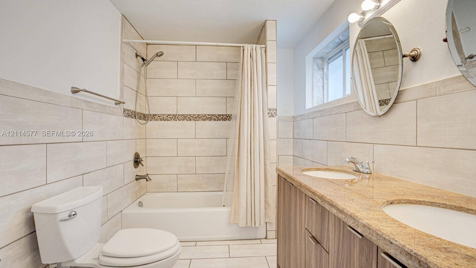 311 SW 38th Court, #0, Miami, Miami, FL 33134 Dual-sink vanity with stone countertop, large-format tile surround, bathtub and shower combination, and oval wall-mounted mirrors