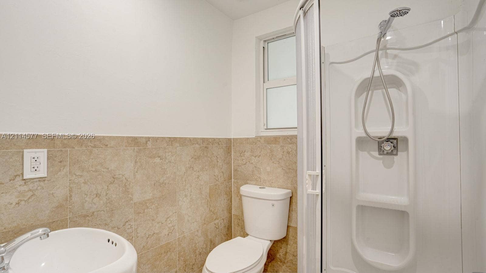 311 SW 38th Court, #0, Miami, Miami, FL 33134 Bathroom featuring large-format beige tile wainscoting, rounded wall-mount basin, white toilet, and enclosed shower stall with built-in shelving