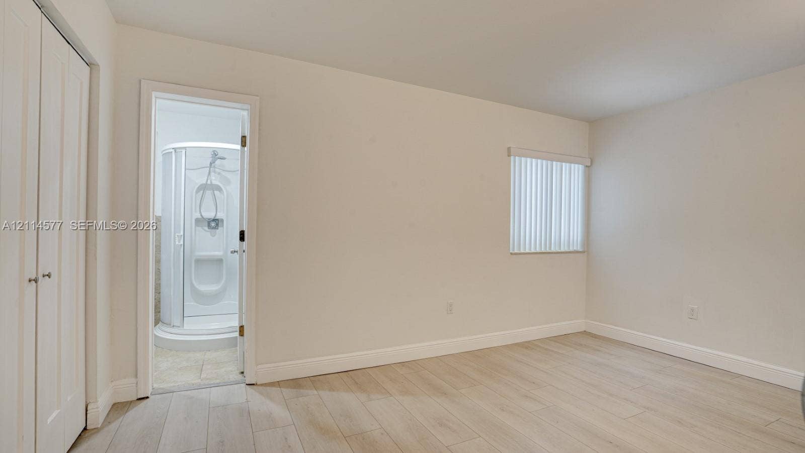 311 SW 38th Court, #0, Miami, Miami, FL 33134 Room featuring wood-finish flooring, white double-door closet, and window with vertical blinds, accompanied by an enclosed shower stall with integrated shelving