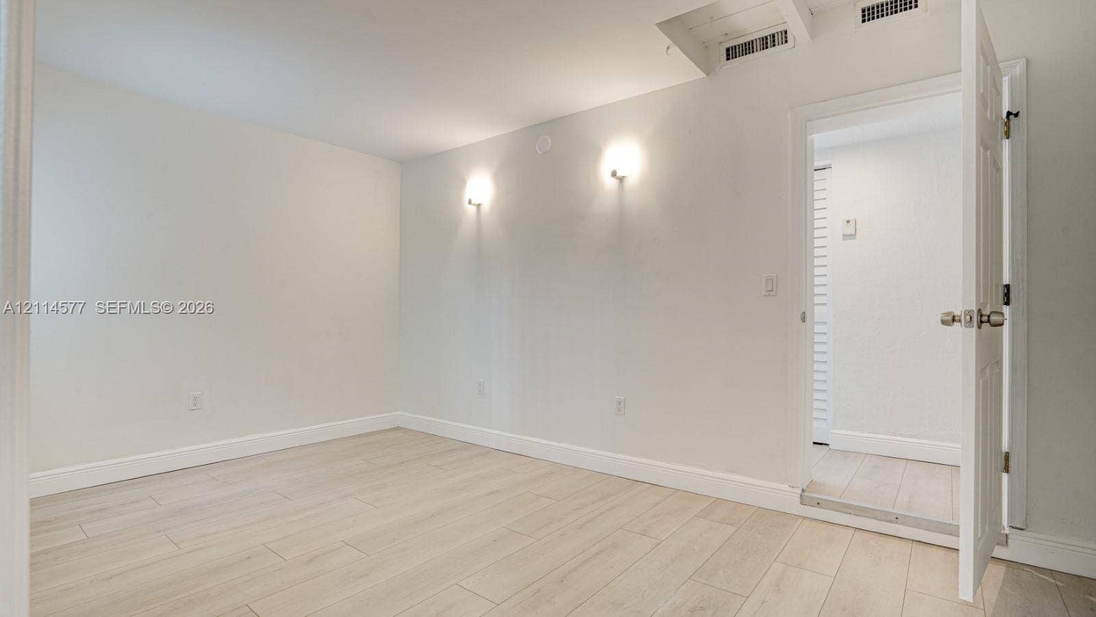 311 SW 38th Court, #0, Miami, Miami, FL 33134 Neutral interior space featuring wood-finish flooring, dual wall-mounted light fixtures, and a six-panel interior door
