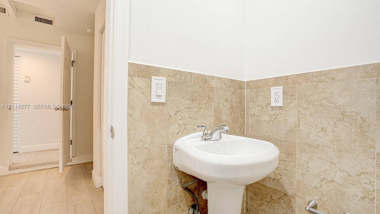 311 SW 38th Court, #0, Miami, Miami, FL 33134 White pedestal sink featuring a dual-handle chrome faucet, complemented by neutral-toned tile wainscoting and light wood-finish flooring
