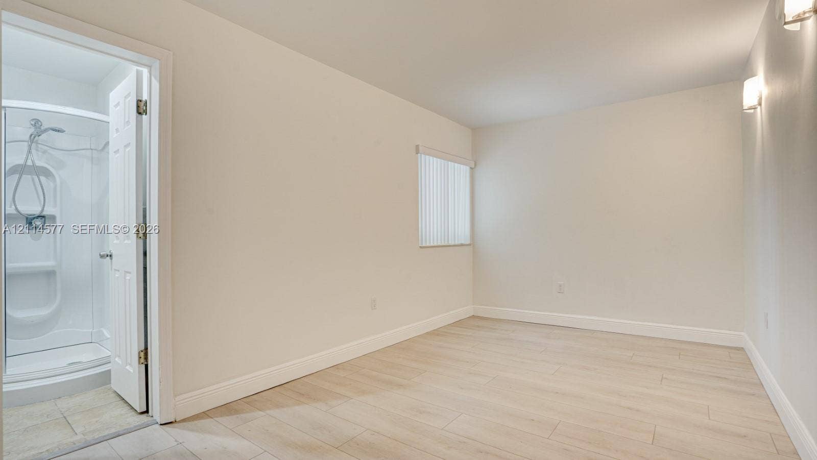 311 SW 38th Court, #0, Miami, Miami, FL 33134 Neutral-toned room with wood-finish flooring, a vertical blind window covering, wall-mounted light fixtures, and a shower stall enclosure with a handheld faucet