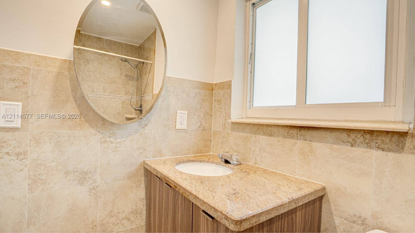 311 SW 38th Court, #0, Miami, Miami, FL 33134 Stone-tiled walls, vanity with stone countertop and integrated sink, oval wall-mounted mirror, and frosted glass window