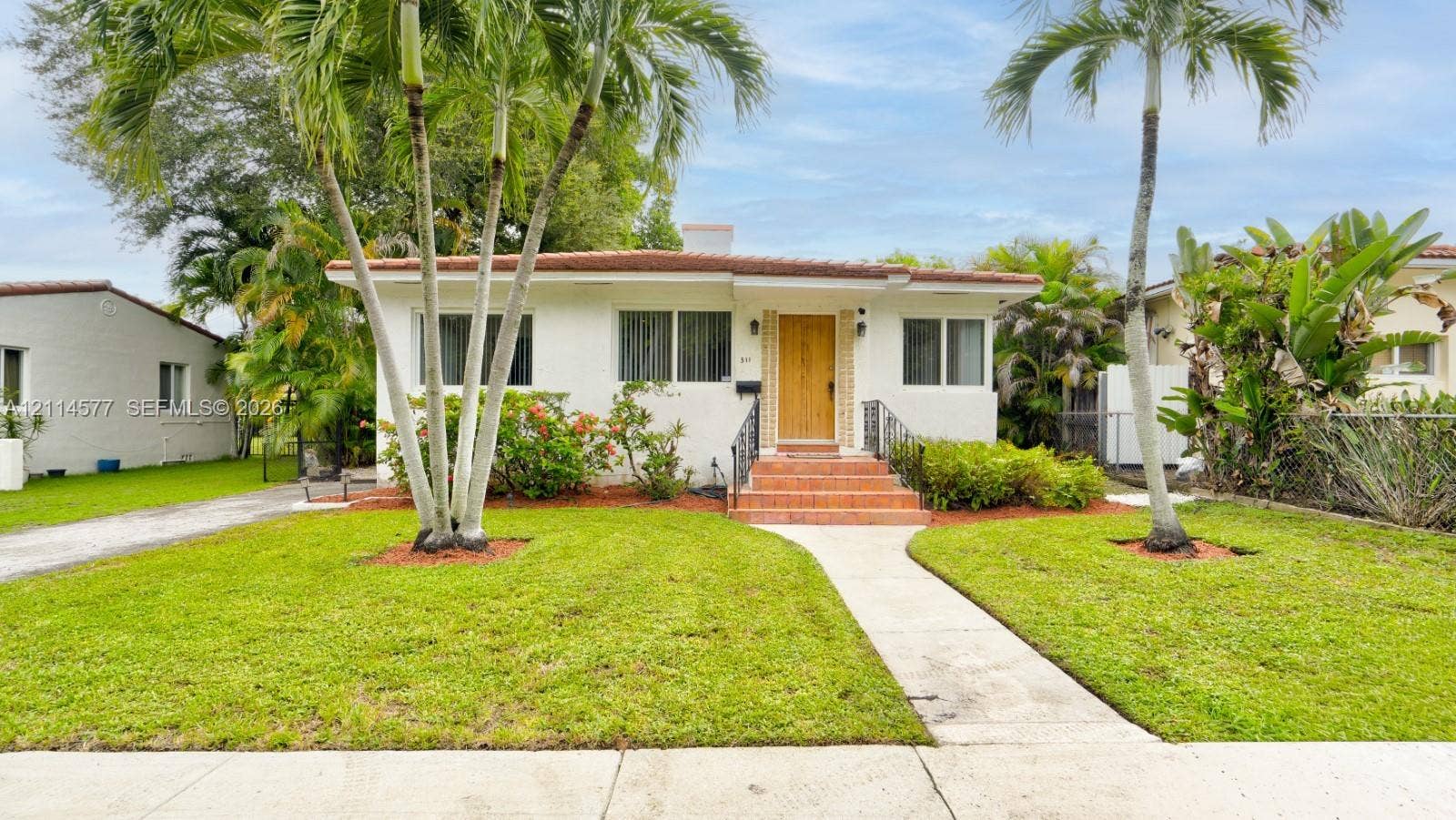 311 SW 38th Court, #0, Miami, Miami, FL 33134 Stucco exterior with a tile roof, natural wood-finish front door, terracotta tiled entry steps, wrought iron handrails, and mature palm landscaping