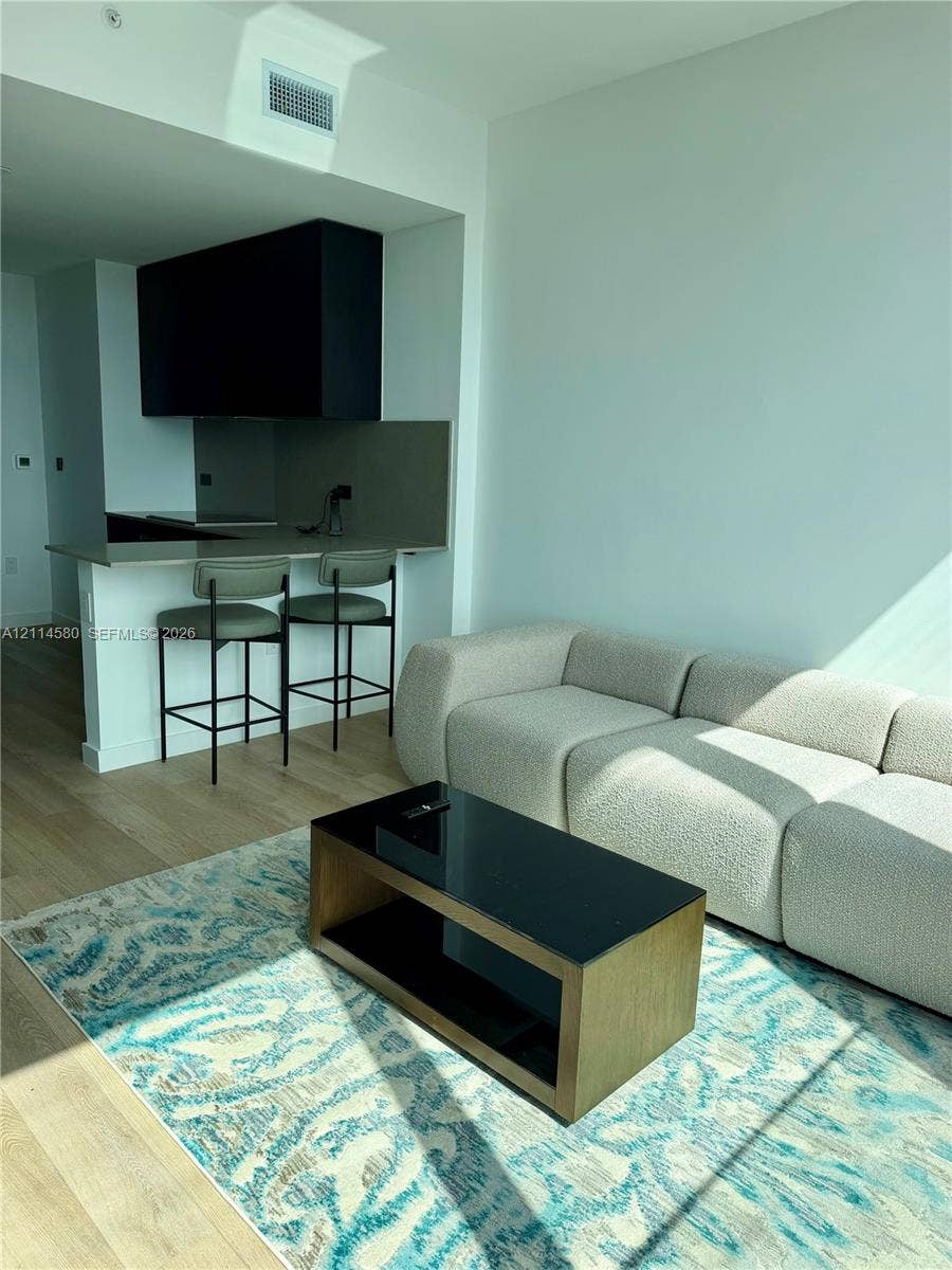 20 NE 11, #4109, Miami, FL 33132 Modern kitchen featuring a sleek peninsula with a solid-surface countertop, matte black cabinetry, and light-toned wood-finish flooring
