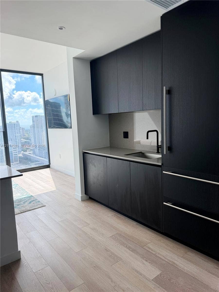 20 NE 11, #4109, Miami, FL 33132 Kitchenette featuring custom matte black cabinetry, quartz countertops, a stainless steel sink with a matte black faucet, integrated appliances, and wood-finish flooring