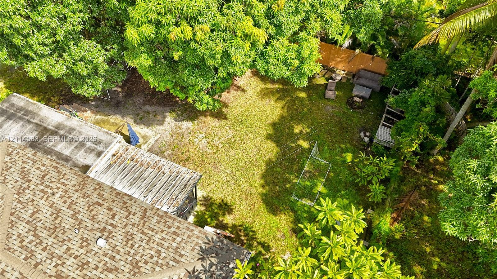 13301 NW Miami Court, Miami, FL 33168 Expansive backyard featuring mature tree canopy, wood-panel fencing, and a shingle-roof structure