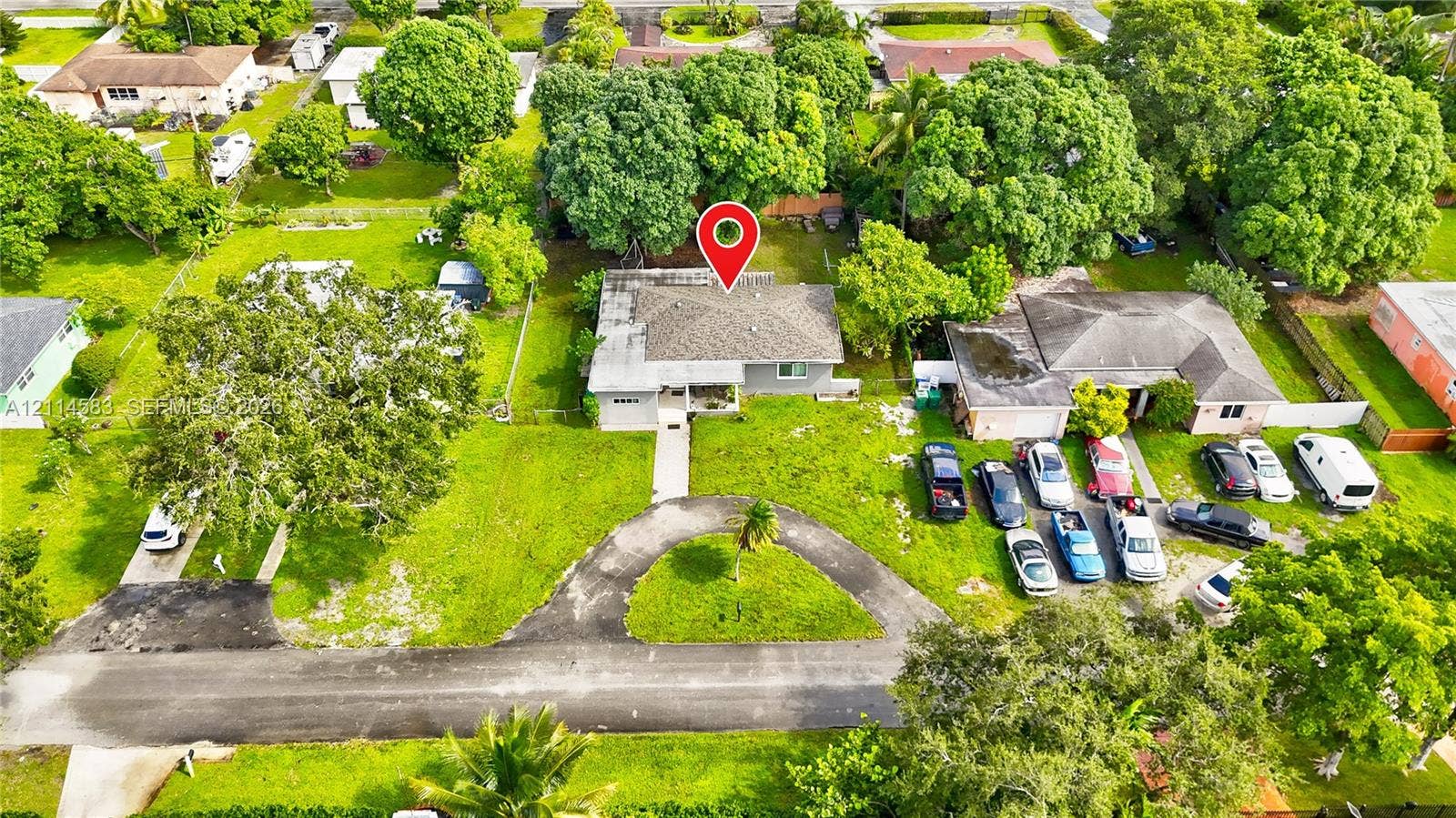 13301 NW Miami Court, Miami, FL 33168 Aerial perspective of a property featuring a hip-roof structure, a circular driveway, and mature landscaping on a spacious lot